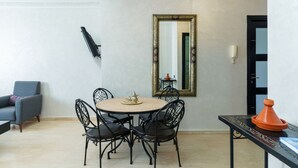 A dining area with a round table, four chairs, a mirror, and a Moroccan tagine on a side table.
