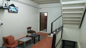 A room with a sofa, a small table, a TV mounted on the wall, and a staircase. - First Inn On Nut - Hostel (Bangkok)