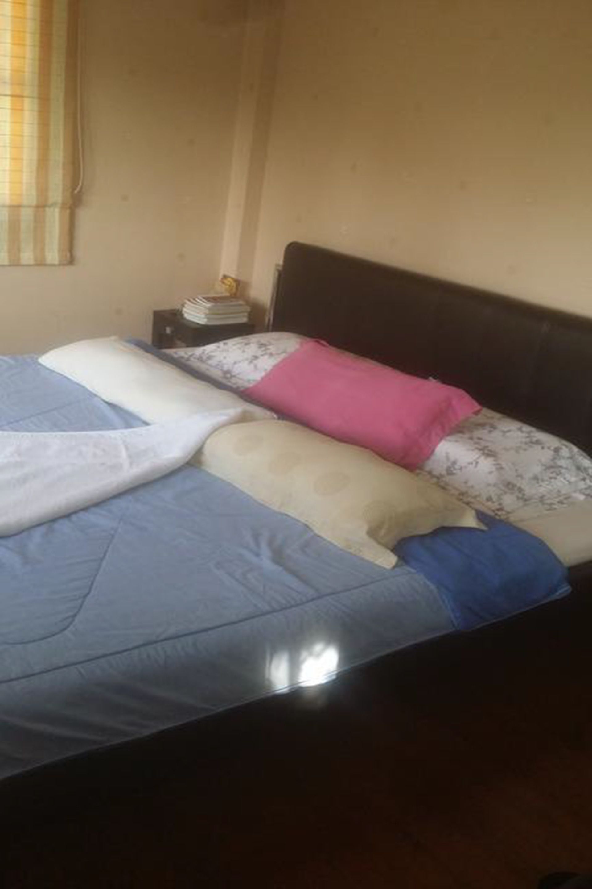 A bed with blue and white bedding, a wooden headboard, and a small bedside table with a lamp and books.