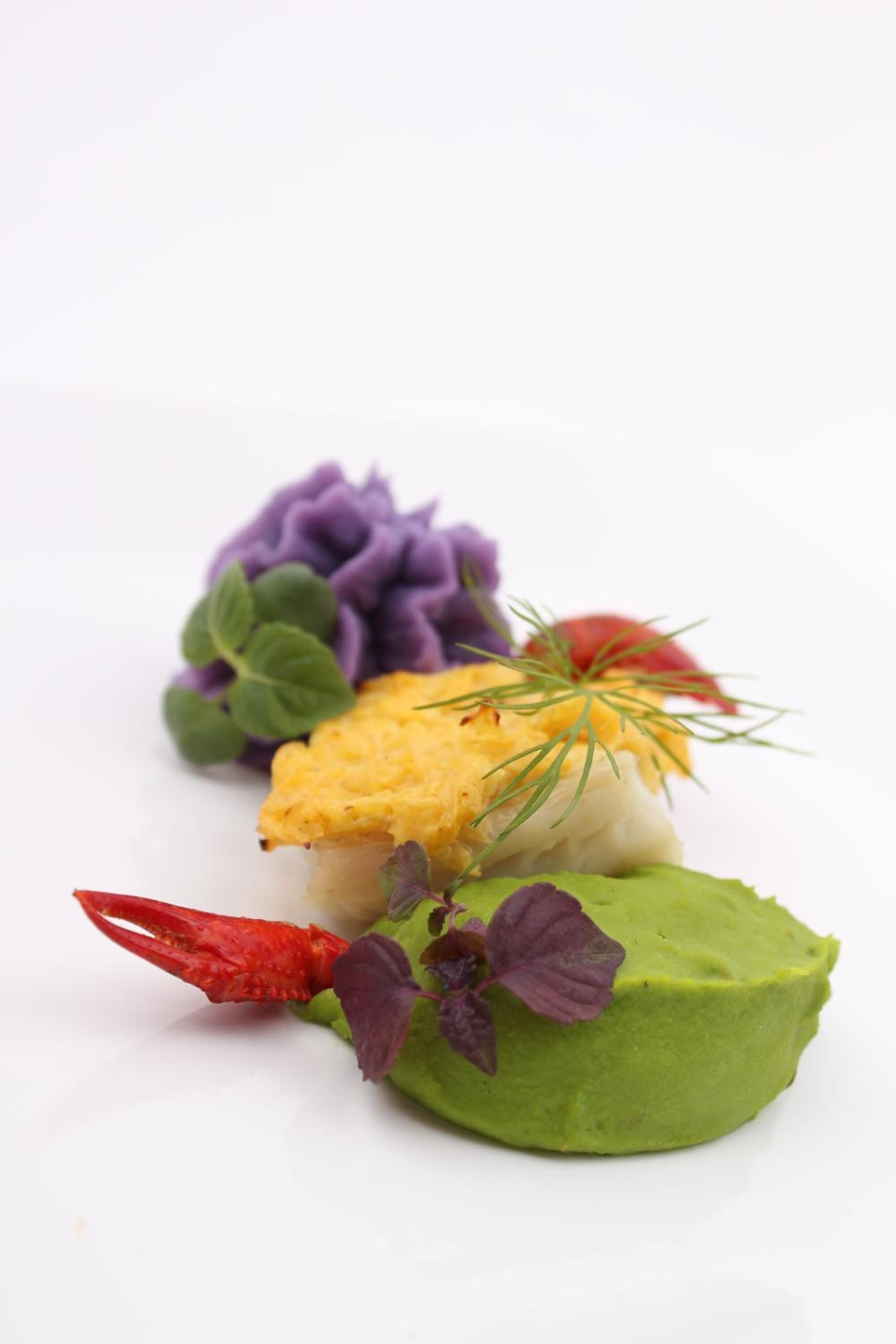 A white plate with a yellow and white food item, green and purple garnishes, and a red chili pepper.
