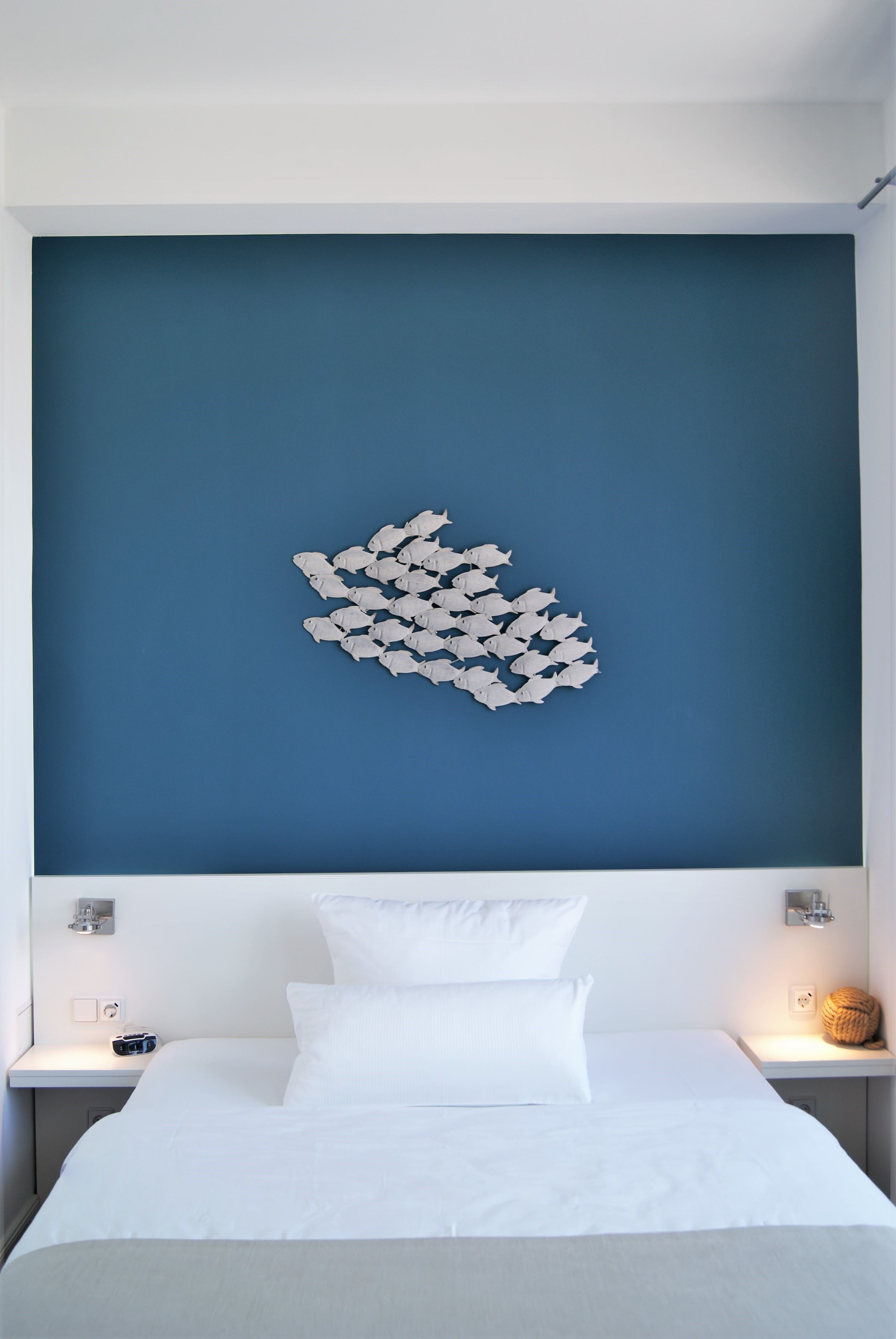 A hotel room with a large bed, a blue accent wall, and a decorative fish wall art piece.