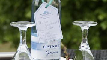 A bottle of Gustrower Gourmet wine with a tag, two clear wine glasses, and a red rose on a white tray.