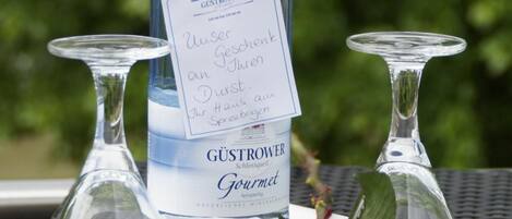 A bottle of Gustrower Gourmet wine with a tag, two clear wine glasses, and a red rose on a white tray.