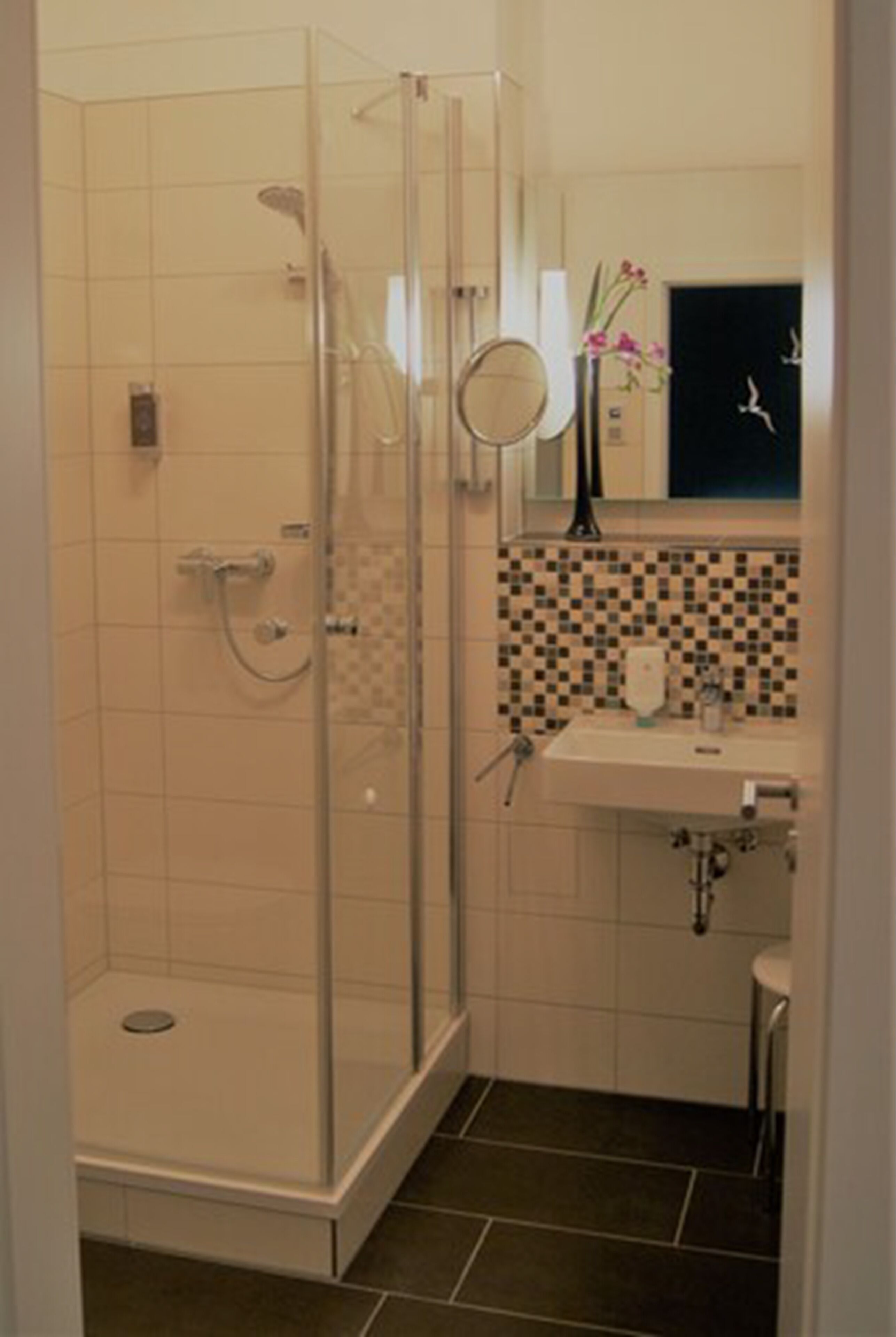 Een badkamer met een douche met glazen wand, betegelde muur, wastafel en spiegel.