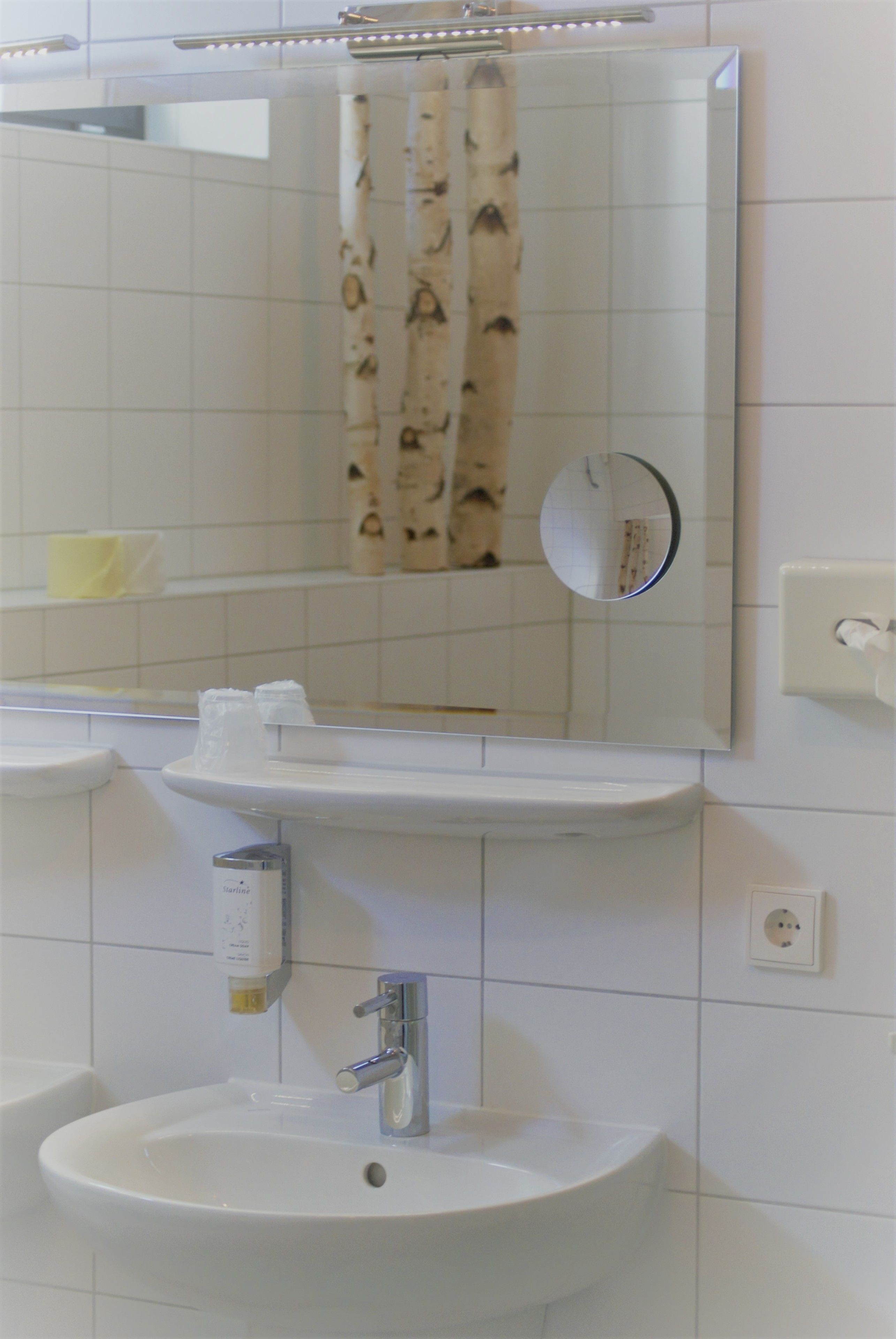 Un baño con lavamanos, espejo y toallero.