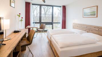 Una habitación de hotel con cama, escritorio, silla y ventana con cortinas.