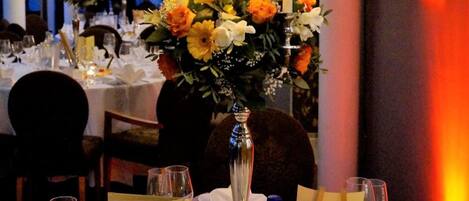 Un espace repas avec des tables dressées pour le repas, des bougies et des centres de table floraux.