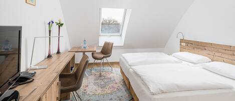 A bedroom with a wooden bed, a desk with a chair, a television, and a window with a view of trees.