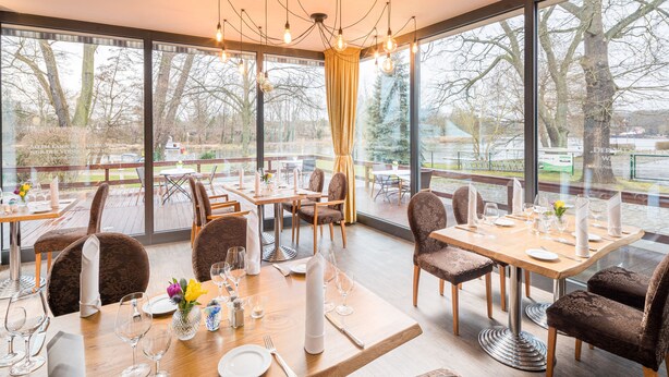 A restaurant with large windows, wooden tables, and brown upholstered chairs.