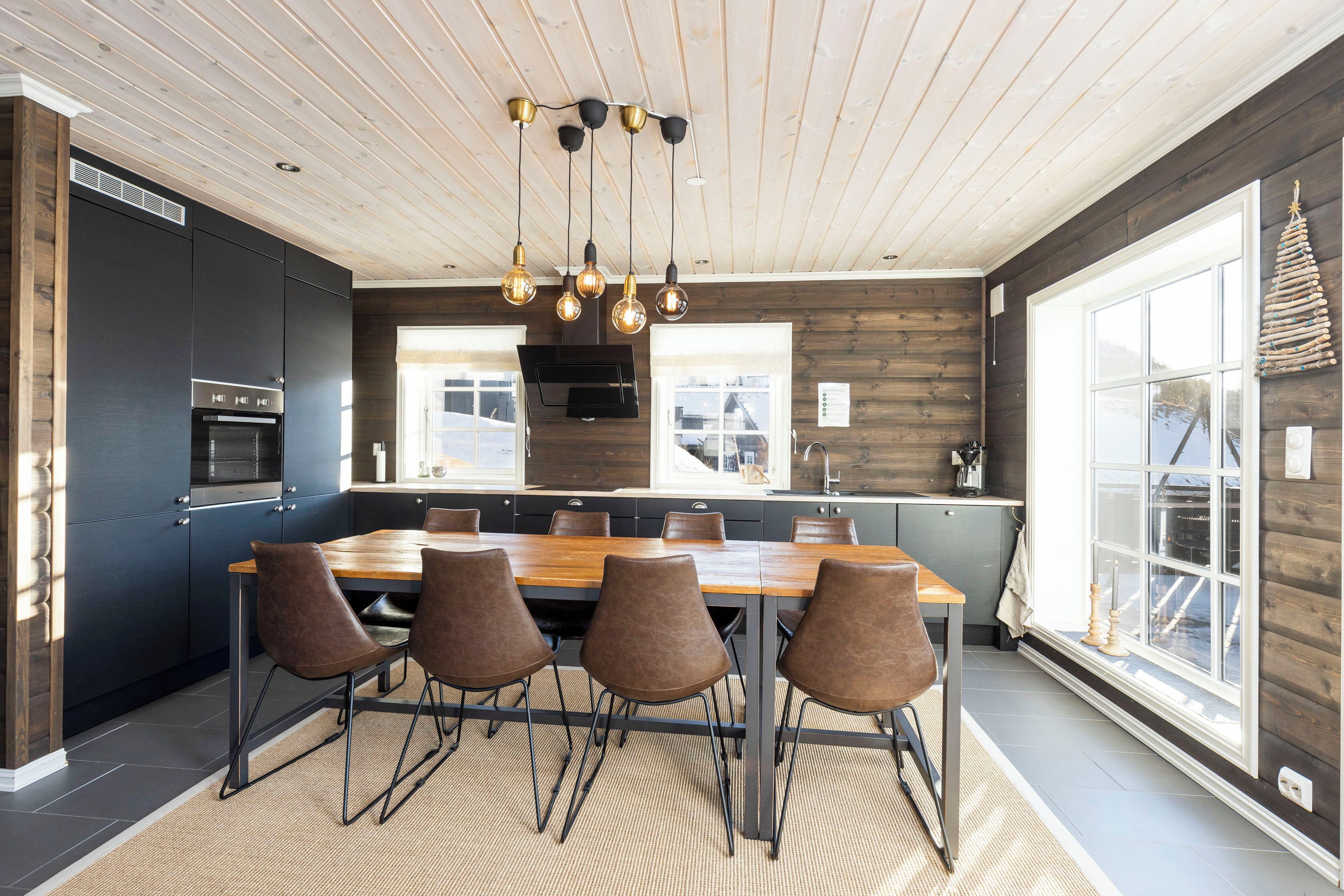 A modern kitchen with a wooden dining table, four chairs, and a hanging light fixture.