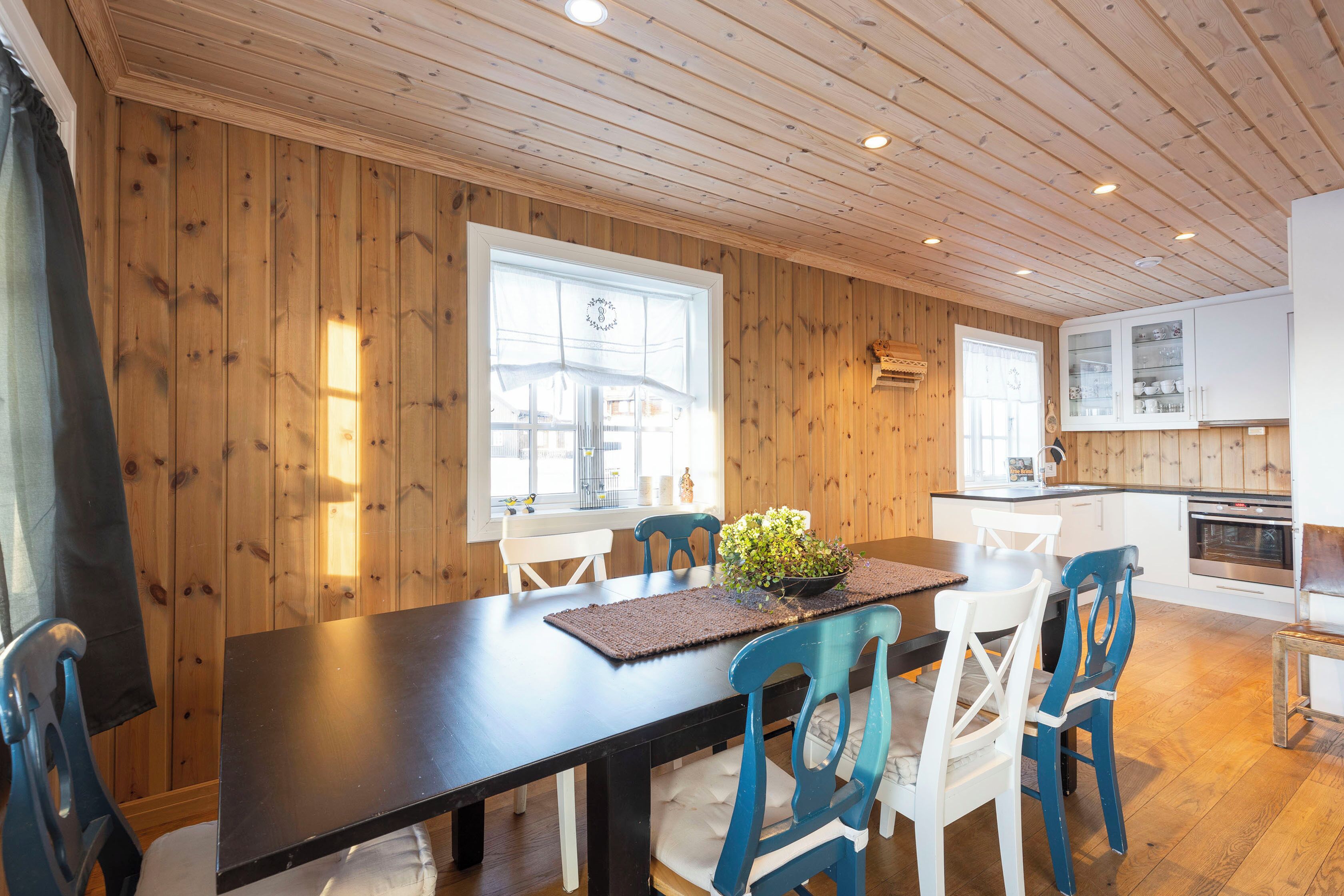 A wooden-paneled room with a dining table, chairs, and a kitchen area.