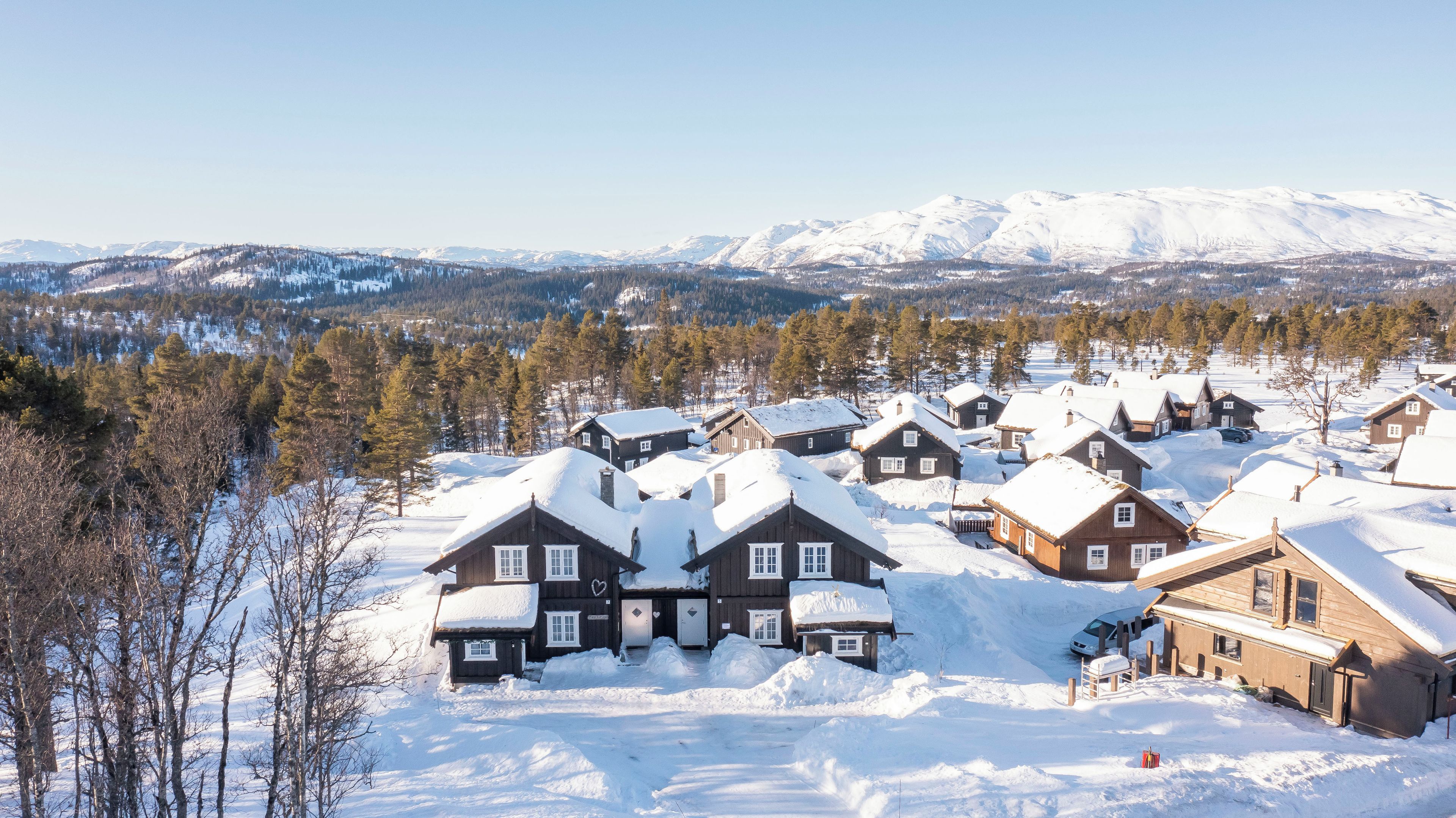 A snow-covered village with wooden houses, a clear sky, and mountains in the background.