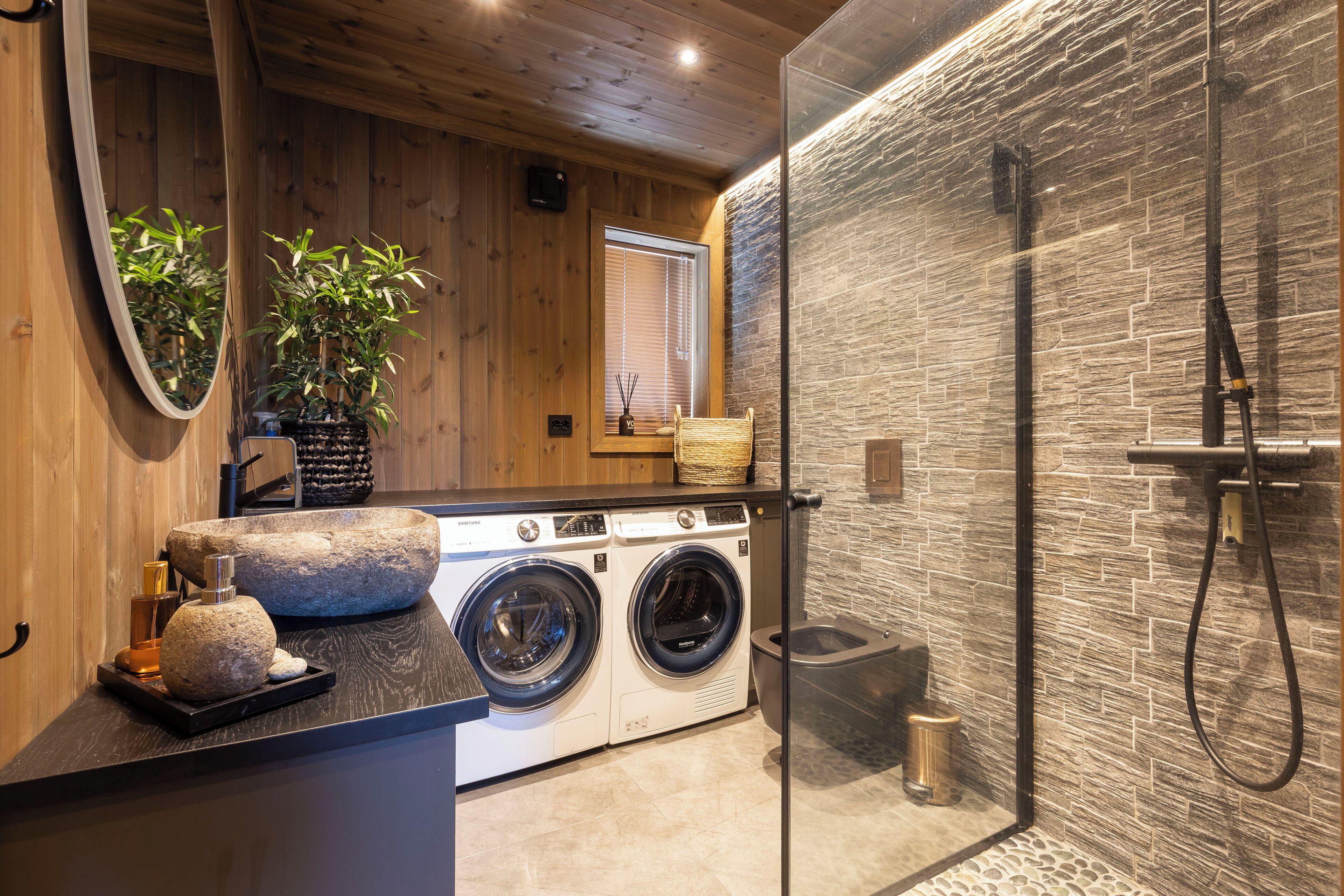Un baño moderno con pared de piedra, cabina de ducha de vidrio y techo de madera.