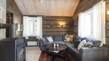 Accogliente interno di una baita in legno con camino in pietra, un divano, un tavolino da caffè e un tappeto decorativo.