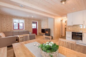 A cozy cabin interior with a wooden interior, a sofa, a dining table, a TV, and a kitchen area.