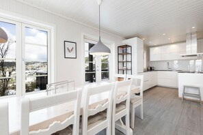Una cocina moderna con armarios blancos, un comedor con sillas blancas y vistas a la ciudad a través de amplios ventanales.