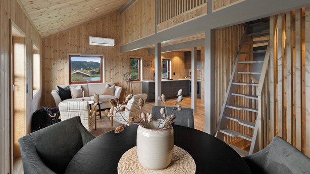 Un interior moderno con paneles de madera, una zona de comedor con mesa negra y un jarrón blanco, y una cocina al fondo.