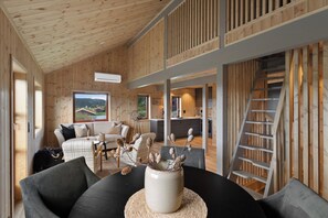 Un interior moderno con paneles de madera, una zona de comedor con mesa negra y un jarrón blanco, y una cocina al fondo.