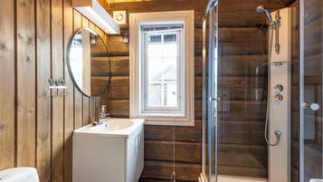 Een houten badkamer in een vakantiehuisje, met een wastafel, spiegel, raam en douche.