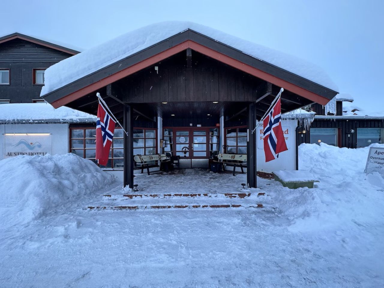 A snow-covered building with a red roof and two flags.