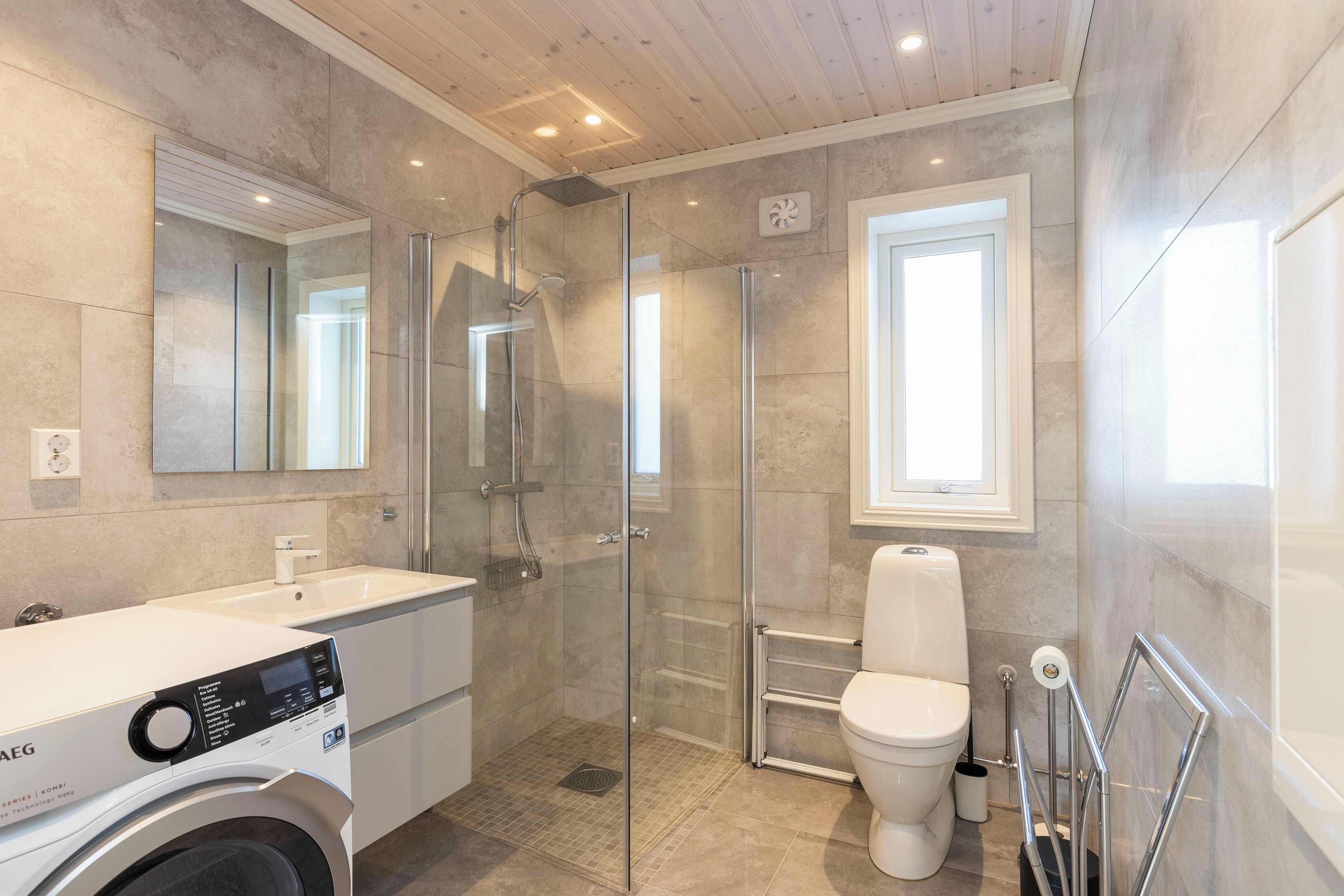 Ein modernes Badezimmer mit einer Glasdusche, einer Toilette und einer Waschmaschine.
