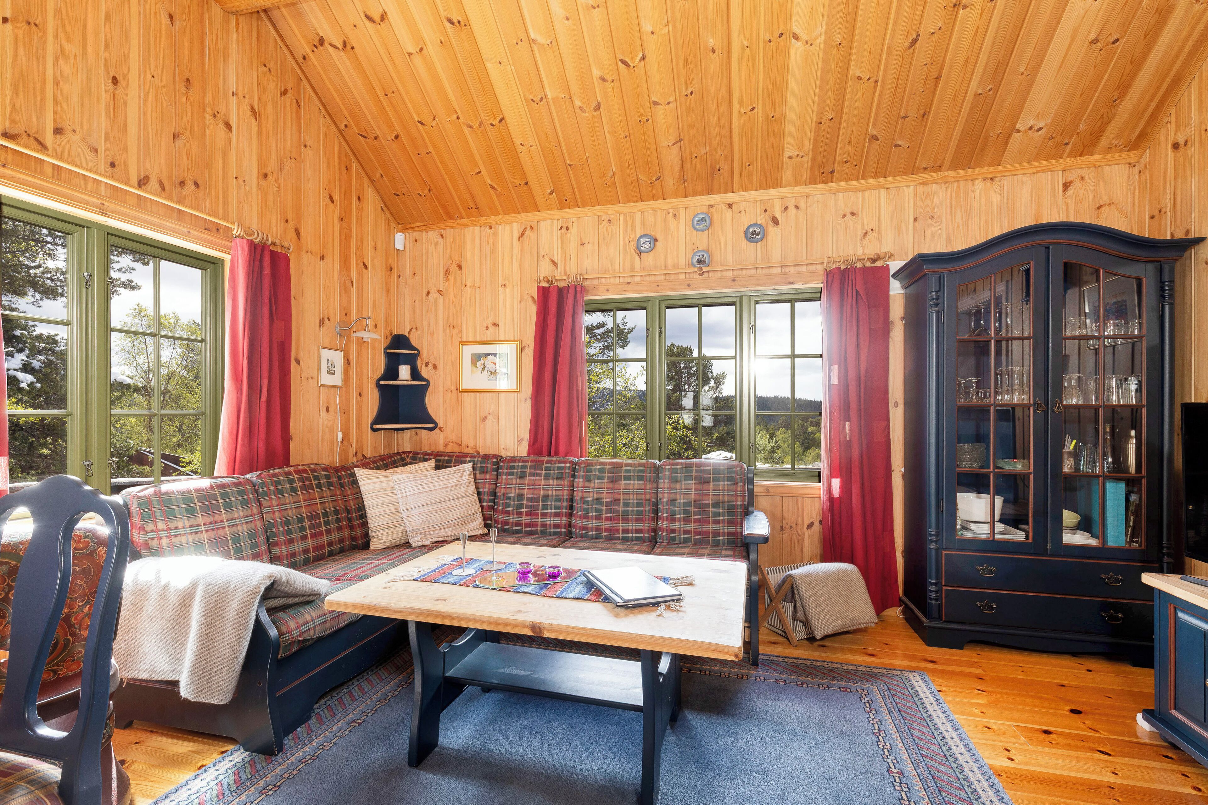 A cozy cabin interior with a plaid sofa, a wooden table, and a dark cabinet.