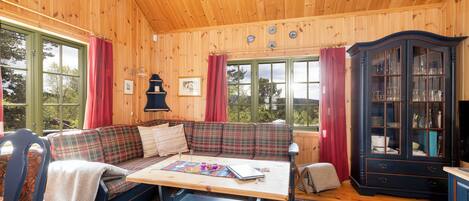 A cozy cabin interior with a plaid sofa, a wooden table, and a dark cabinet.