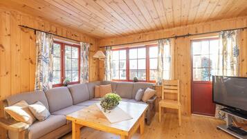 A wooden cabin interior with a sofa, a coffee table, a television, and large windows.
