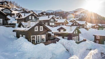 A cluster of wooden cabins with snow-covered roofs, surrounded by a mountainous landscape.
