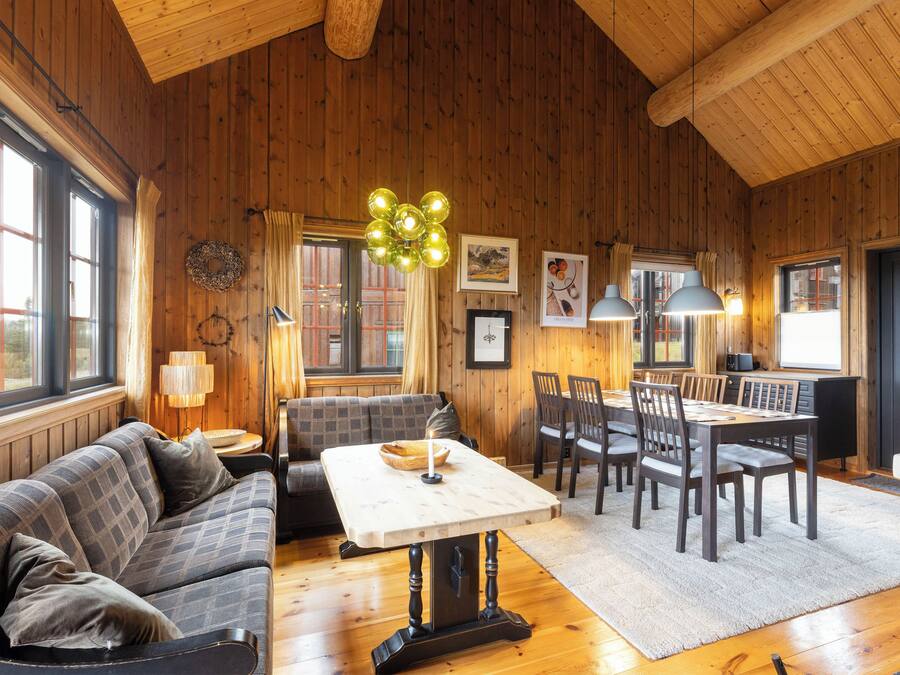 A cozy room with a wooden ceiling, a dining table with chairs, a sofa, and a fireplace.