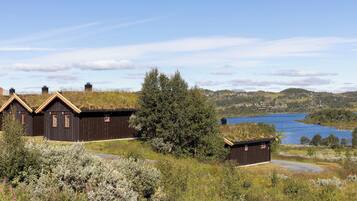 A row of traditional wooden houses with grass roofs, surrounded by natural vegetation and a lake in the background.