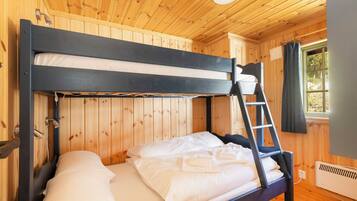 Uma cama de beliche com escada, paredes de madeira, uma janela com cortinas e um radiador.