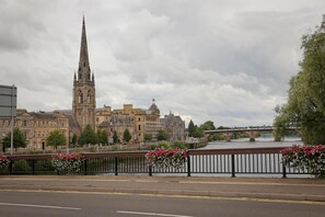 A historic building with a tall spire, a river, and a bridge in the background.