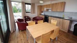 Une cuisine moderne avec des meubles en bois, une table à manger avec quatre chaises et une vue sur la rue par la fenêtre.