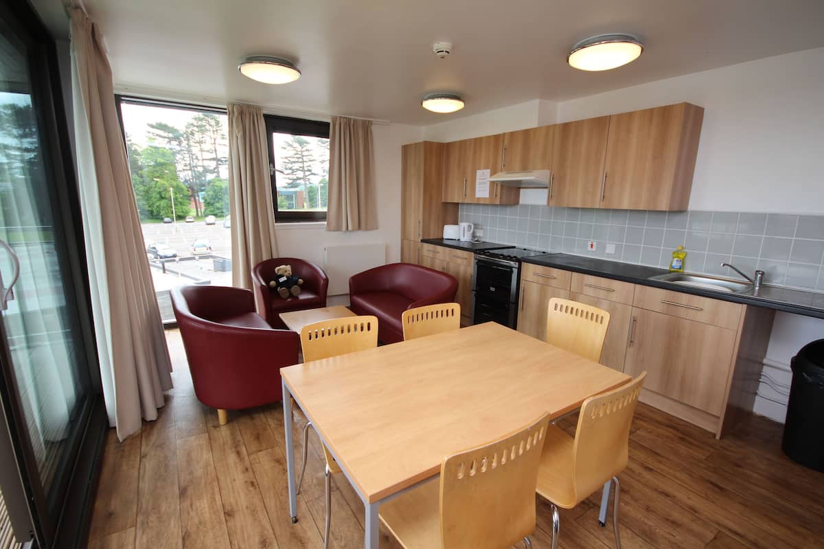 A modern kitchen with wooden cabinets, a dining table with four chairs, and a view of the street through the window.