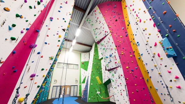 Une salle d’escalade intérieure dotée de plusieurs murs d’escalade, d’un sol rembourré et de cordes de sécurité.