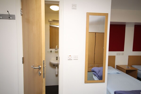 A hotel room with a wooden door, a mirror, a sink, and two beds with blue bedding. - Perth Youth Hostel (Perth)