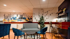 Un vestíbul d'hotel modern amb un sofà gris, butaques blaves, una taula rodona petita i un mural decoratiu a la paret.