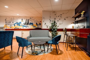 Un moderno vestíbulo de hotel con un sofá gris, sillones azules, una mesita redonda y un mural decorativo.