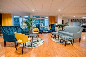 Un hallo amplio con suelo de madera y diversas opciones de asiento, incluyendo un sillón azul, una silla amarilla y un sofá gris.