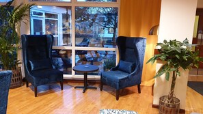 A cozy seating area with two blue armchairs and a small round table, a large window with a view of the outside, and a potted plant. - Inverness Youth Hostel (Inverness)