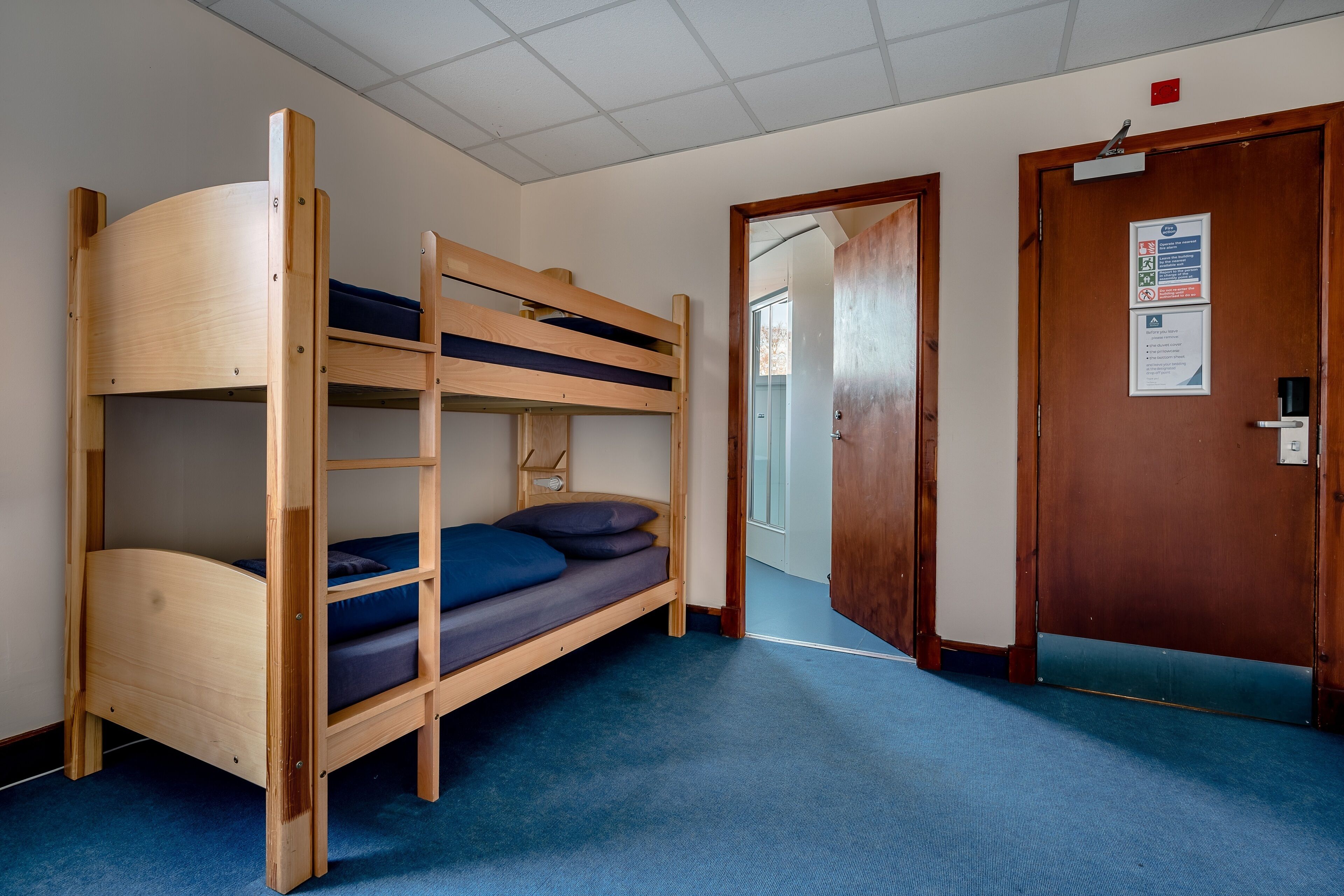 A bunk bed room with a blue carpet, wooden door, and a sign on the wall.