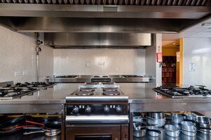Una cocina industrial con electrodomésticos de acero inoxidable, incluyendo múltiples hornillas y una campana extractora grande.