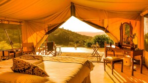A tented accommodation with a bed, desk, chair, and a view of the landscape. - Entumoto Safari Camp (Maasai Mara)