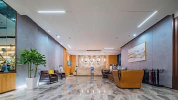 A hotel lobby with a reception desk, seating area, and a large potted plant.
