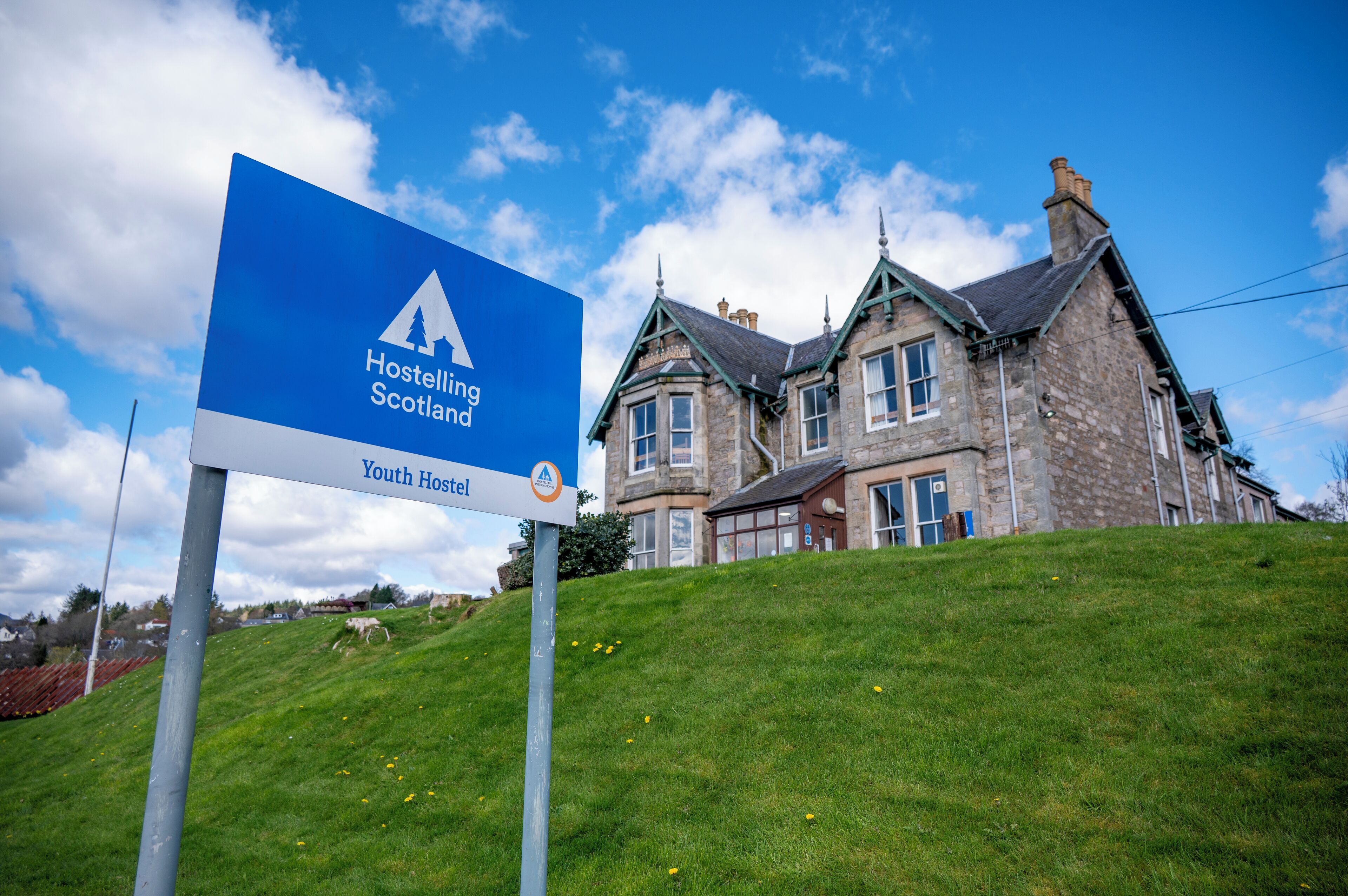 Segnaletica per l'ostello della gioventù Hostelling Scotland, con un edificio in pietra sullo sfondo.