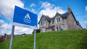 Segnaletica per l'ostello della gioventù Hostelling Scotland, con un edificio in pietra sullo sfondo.