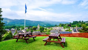 A picnic area with two wooden benches and a flagpole, overlooking a village with historic buildings and a church. - Pitlochry Youth Hostel (Pitlochry)