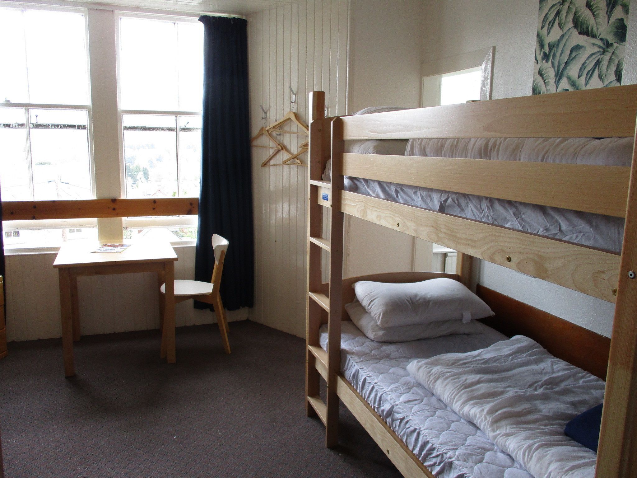 A bunk bed room with a desk and chair, a window with curtains, and a wall with a tropical print.