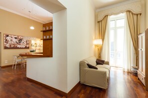 A living room with a sofa, a dining area with a table and chairs, and a kitchen area with shelves and a hanging light. - Residenza Duomo 314 (Naples)